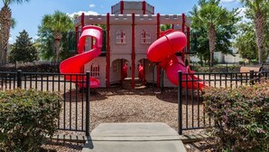 Ein spielplatz im Burgstil mit zwei roten Rutschen und einer Burgfassade.