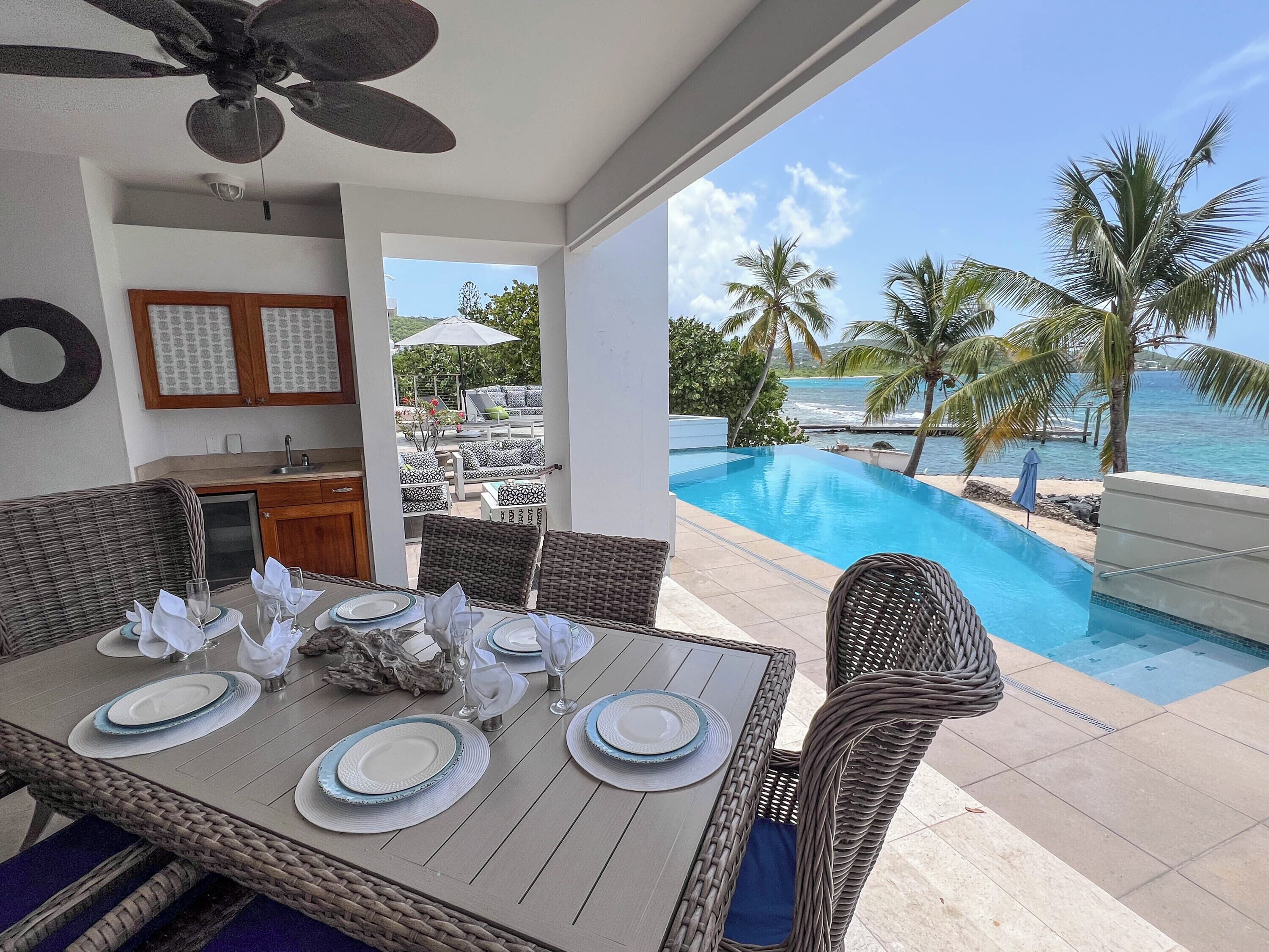 Comedor con mesa dispuesta para seis personas, con vistas a una piscina y palmeras.