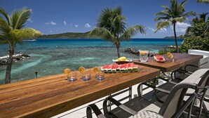 A wooden table with a tropical view, a watermelon, and a drink tray. - "ONE BEACH ROAD Villa", St Thomas VI, 6 Bedroom, 5 1/2 Bath Beachfront Oasis (St. Thomas)