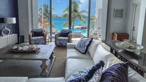 A living room with a white sofa, two armchairs, a coffee table, and a view of the ocean through large sliding glass doors. - "ONE BEACH ROAD Villa", St Thomas VI, 6 Bedroom, 5 1/2 Bath Beachfront Oasis (St. Thomas)