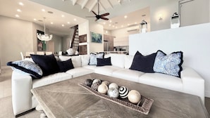 A modern living room with a sectional sofa, a coffee table with decorative items, ceiling fans, recessed lighting, and a kitchen in the background. - "ONE BEACH ROAD Villa", St Thomas VI, 6 Bedroom, 5 1/2 Bath Beachfront Oasis (St. Thomas)