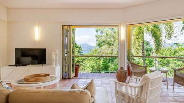 A living room with a TV, sofa, and a balcony with outdoor furniture. - The Hill Villa 2 Port Douglas (Port Douglas)