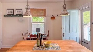 A dining area with a wooden table, two hanging pendant lights, a window with blinds, and a door. - GOOD VIBES IS WHAT YOU'LL FEEL WHEN YOU STEP IN TO OUR FAMILY FRIENDLY LISTING (Cape Charles)