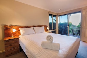 A hotel room with a large bed, two bedside lamps, a wooden headboard, a window with a view, and a balcony with outdoor furniture. - Views Of The Bay—A Tranquil Bushland Escape (Yallingup Siding)