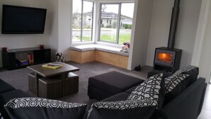 A living room with a sofa, a coffee table, a flat-screen TV, a fireplace, and large windows offering a view of the outside. - Family Executive House (Pohara)
