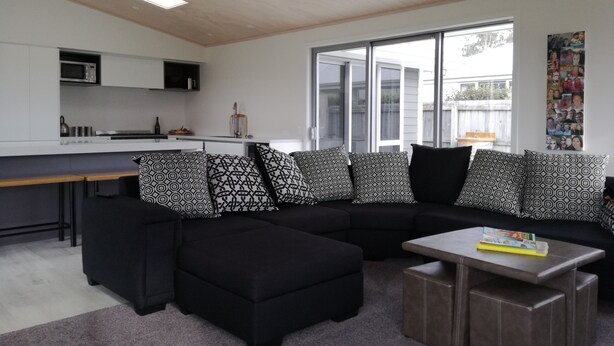 A modern living room with a black sectional sofa, a coffee table, and a kitchen area with white cabinets and a microwave. - Family Executive House (Pohara)