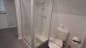 A bathroom with a glass-enclosed shower, a toilet, and a roll of toilet paper on the wall. - Evergreen - spacious family retreat, so close to shops and beaches. (Venus Bay)
