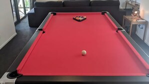 A pool table with a red felt surface, a white cue ball, and a set of billiard balls in the center. - Evergreen - spacious family retreat, so close to shops and beaches. (Venus Bay)