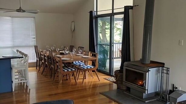 A dining area with a wooden table and chairs, a ceiling fan, and a wood-burning stove. - Evergreen - spacious family retreat, so close to shops and beaches. (Venus Bay)