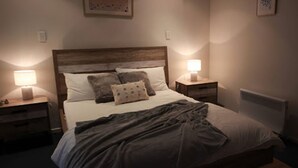 A neatly made bed with a wooden headboard, two bedside tables with lamps, and a radiator on the wall. - Evergreen - spacious family retreat, so close to shops and beaches. (Venus Bay)