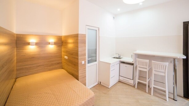 A compact room with a bed, a small kitchenette, and a desk with two chairs. - Smart Apartment Zamarstinivska 20a (Lviv)