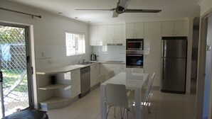 A modern kitchen with white cabinets, stainless steel appliances, and a dining area with a white table and chairs. - Palmgrove 1 - Rainbow Beach. Gorgeous, modern beach escape in a great location. Aircon. Wifi (RAINBOW BEACH)