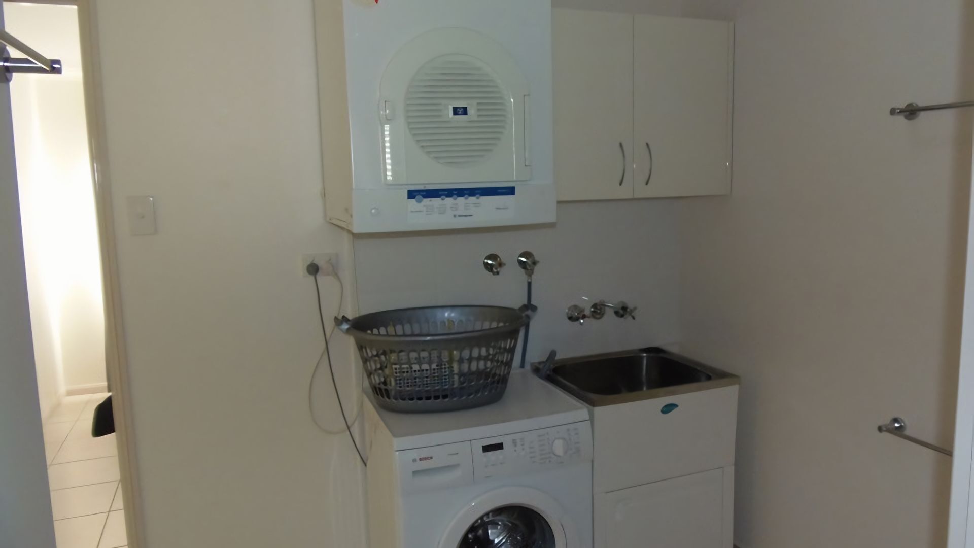 Un área de lavandería compacta con lavadora, secadora, lavabo y tendedero.
