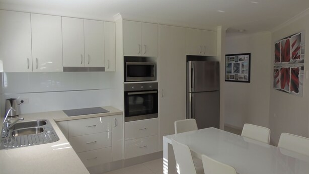 A modern kitchen with white cabinetry, a stainless steel refrigerator, an oven, and a microwave. There is a dining table with chairs. - Palmgrove 1 - Rainbow Beach. Gorgeous, modern beach escape in a great location. Aircon. Wifi (RAINBOW BEACH)
