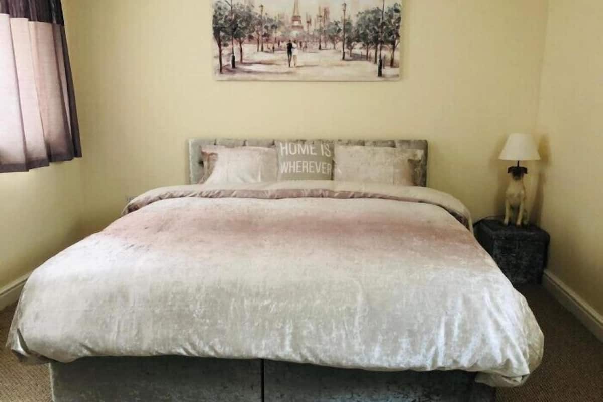 Une chambre à coucher avec un lit, une tête de lit agrémentée d’oreillers, un tableau au mur et une lampe sur une table de chevet.
