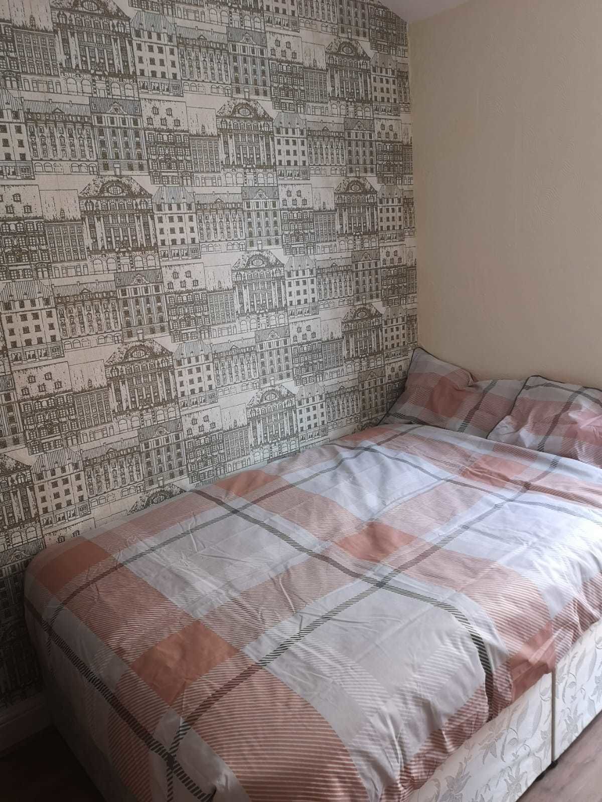 A room with a bed featuring a checkered bedspread and a wall with a detailed cityscape wallpaper.