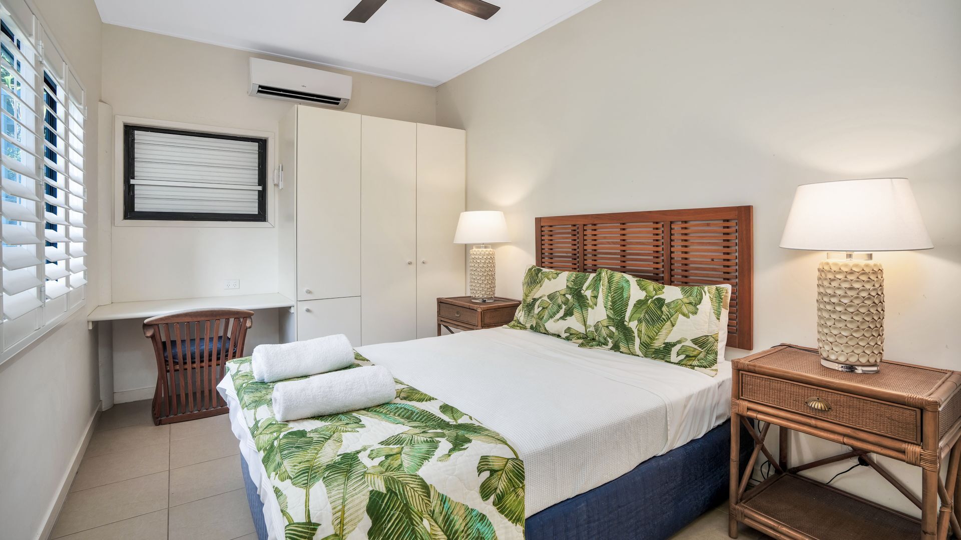Un dormitorio con cama, escritorio, silla, armario y dos lámparas de noche.