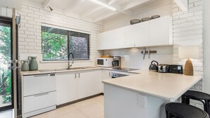 A modern kitchen with white cabinetry, a built-in microwave, a kettle, and a coffee maker.