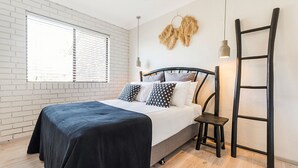 A bedroom with a bed, a window with blinds, a wall-mounted lamp, and a ladder.
