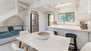 A modern kitchen with a white countertop, a dining table with four chairs, a refrigerator, and a window with blinds.