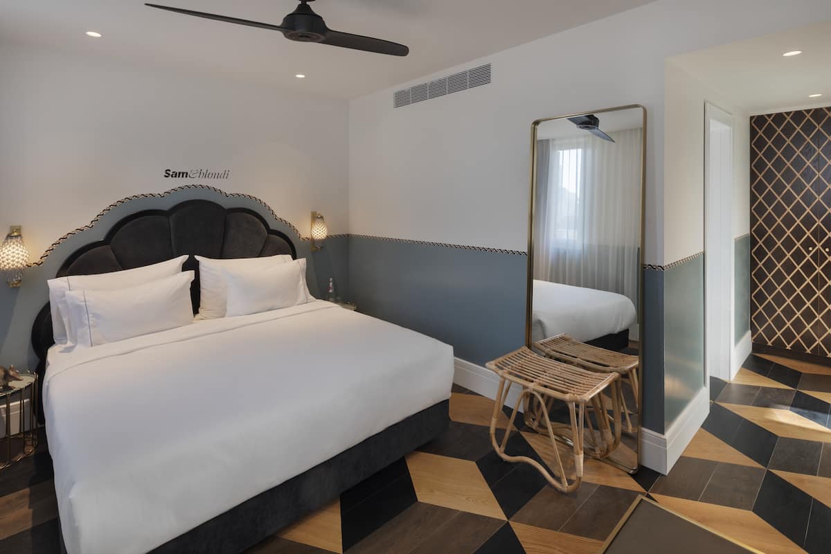 A hotel room with a bed, a ceiling fan, a mirror, and a patterned floor.
