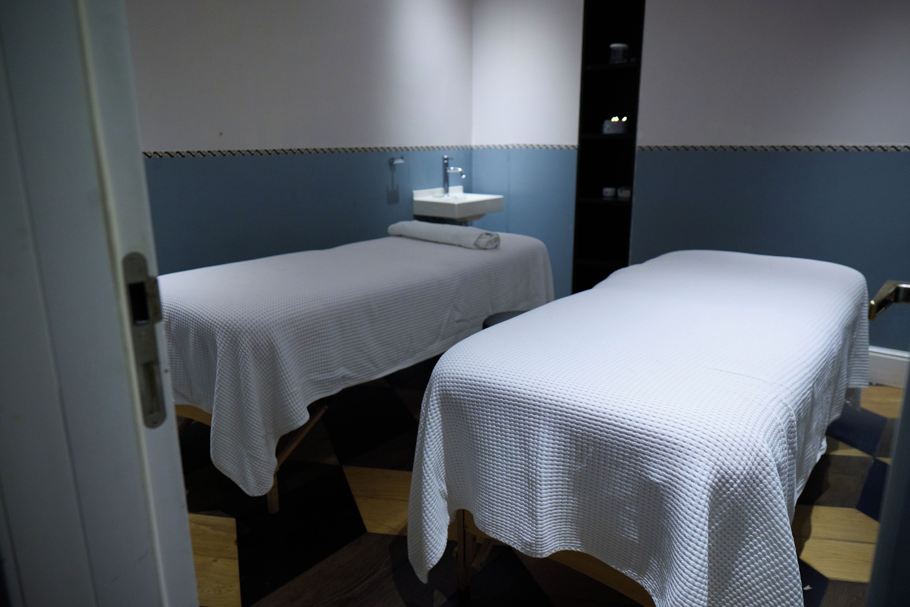 Una habitación con dos camas cubiertas con sábanas blancas, un lavabo y un espejo en la pared.