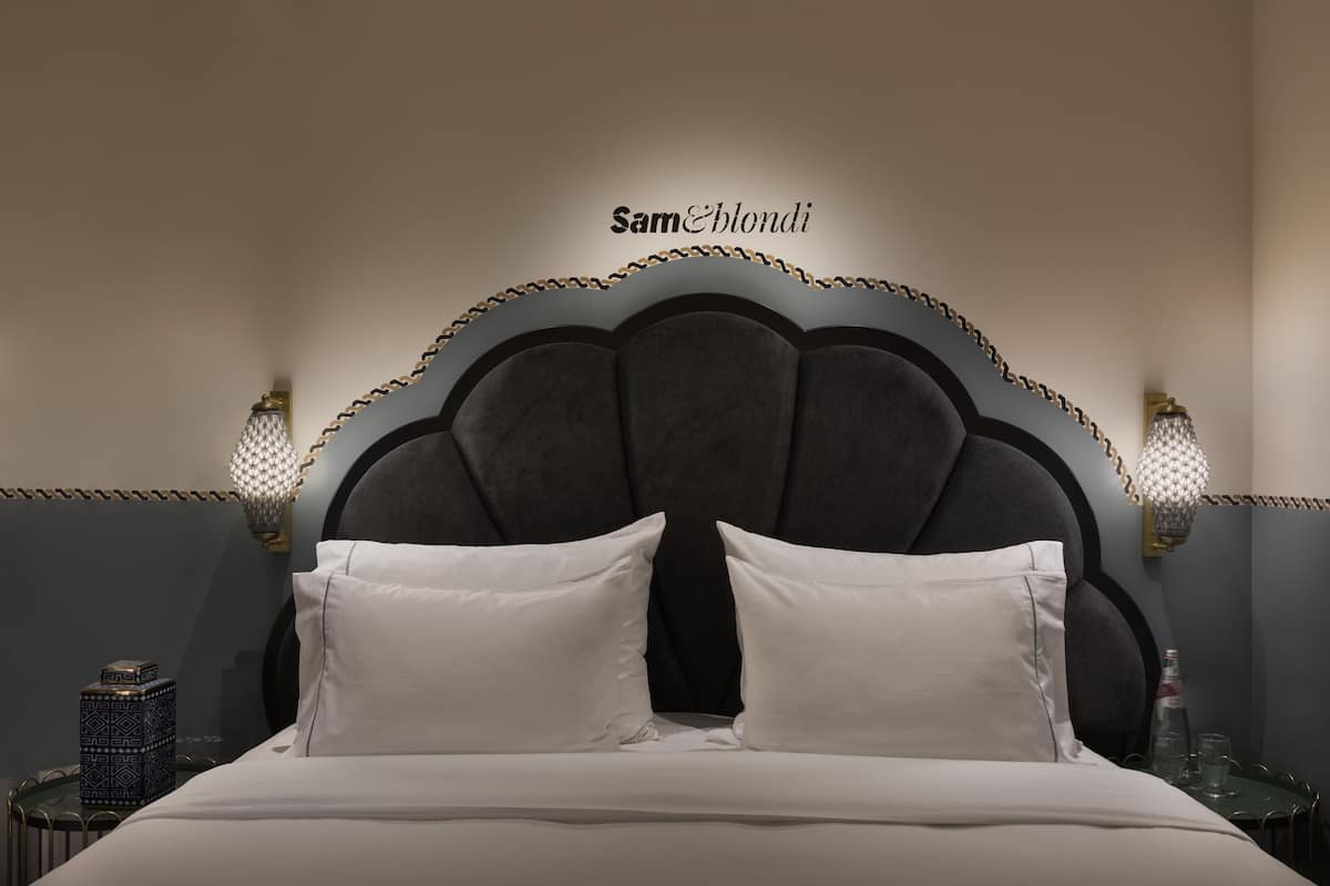A neatly made bed with white linens and a dark, ornate headboard.