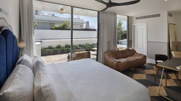 Habitación de hotel moderna con una cama grande, un sofá de cuero, una mesa de comedor y un balcón con plantas.