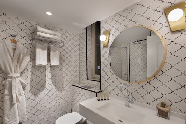 A bathroom with a white sink, a round mirror with a gold frame, and a towel rack with folded towels. - Sam & Blondi (Tel Aviv)