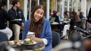 A person seated at an outdoor cafe with a plate of food and a drink.