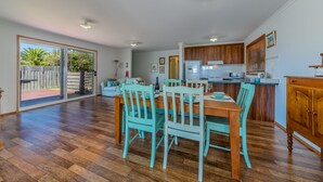 Une cuisine spacieuse avec des meubles en bois, un coin repas avec des chaises turquoise et une porte-fenêtre coulissante donnant sur un patio.