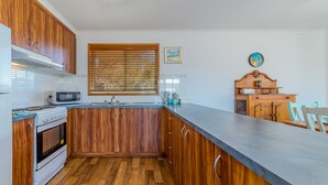 Une cuisine avec des meubles de rangement en bois, un four à micro-ondes, une cuisinière et une fenêtre avec des stores.