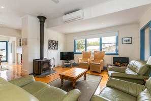 A living room with a fireplace, two armchairs, a sofa, a television, and a large window. - Sand, Surf & Sunshine (Anglesea)