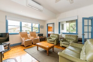 A spacious living room with a television, two wicker chairs, a leather sofa, and a coffee table.