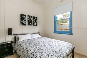 A bedroom with a bed, a nightstand, a lamp, and a window with blue trim.