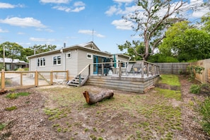 A single-story house with a deck, a fenced backyard, and a large tree. - Sand, Surf & Sunshine (Anglesea)