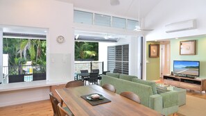 Relax in this open-plan living space with a dining area and seating area, offering a view of the lush tropical garden.