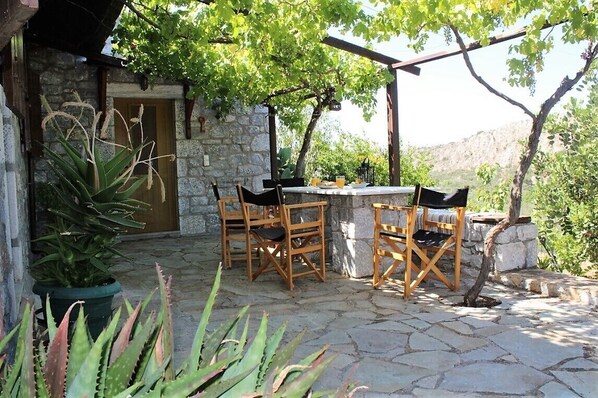 Un patio al aire libre con suelo de piedra, sillas de madera y una mesa.