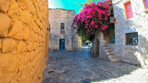 Une ruelle étroite pavée, bordée de bâtiments en pierre, avec une porte bleue et une enseigne indiquant « Hôtel ».