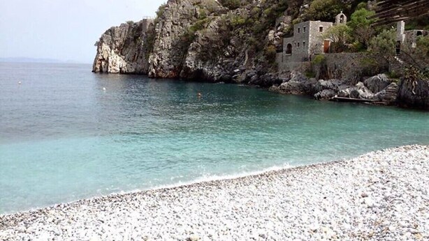 Une côte rocheuse avec une plage de galets et un bâtiment doté d’un clocher.