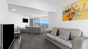 A modern living room with a sofa, a flat-screen TV, and a painting. - Grande Corniche U17 - Panoramic Kirra Hill (Kirra)