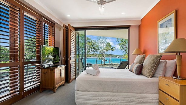 A bedroom with a large bed, a TV, and a view of the sea.