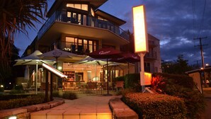 A two-story building with outdoor seating and umbrellas, a well-lit entrance, and a visible sign.