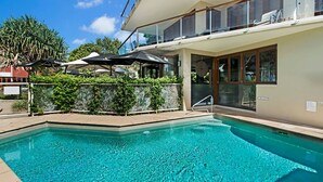 A swimming pool with a glass balustrade, surrounded by a landscaped area with plants and umbrellas.