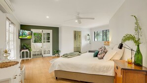 Ein Schlafzimmer mit Bett, Schreibtisch, Stuhl, Fernseher und einem Fenster mit Jalousien.