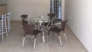 A dining area with a glass-top table and wicker chairs, a tiled floor, and a door leading to another room. - Recanto da Bia, 3 bedrooms, air conditioning, Wi-Fi and 4 minutes from the park. (Olímpia)