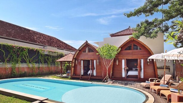 Un área junto a la piscina con piscina, cabañas de madera y sillas de descanso.