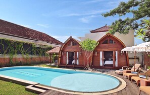 A poolside area with a swimming pool, wooden cabins, and lounge chairs. - Kubu GWK Resort (Jimbaran)