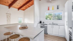 Een moderne keuken met witte kasten, een houten kookeiland met krukken, een raam met uitzicht op groen en een plafond met zichtbare houten balken.