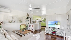 Een moderne woonkamer met een bank, salontafel en een televisie. Er is een keuken met groene kastjes en een eettafel.